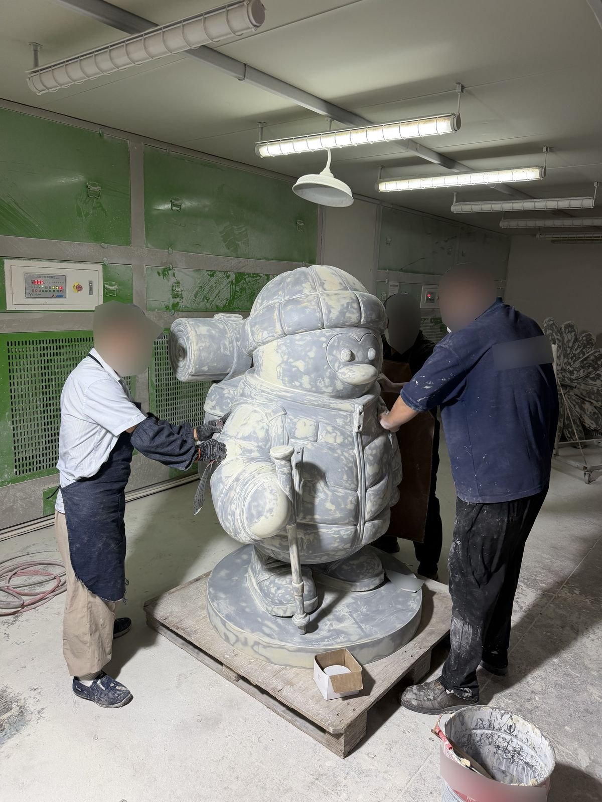 Workers sanding the surface of a custom mascot sculpture with sculpted clothing details