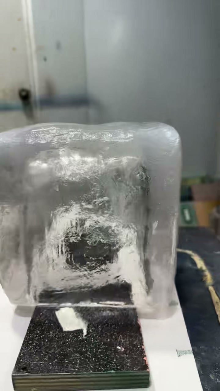 Transparent ice cube prop resting on a black support