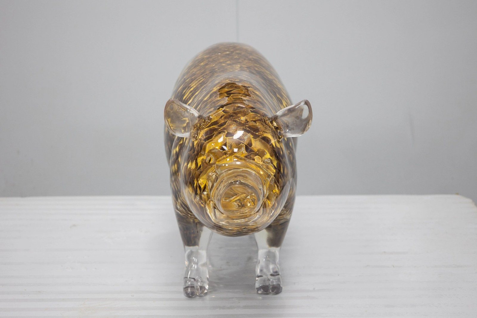 Front view of a transparent pig display sculpture with gold-tone detail